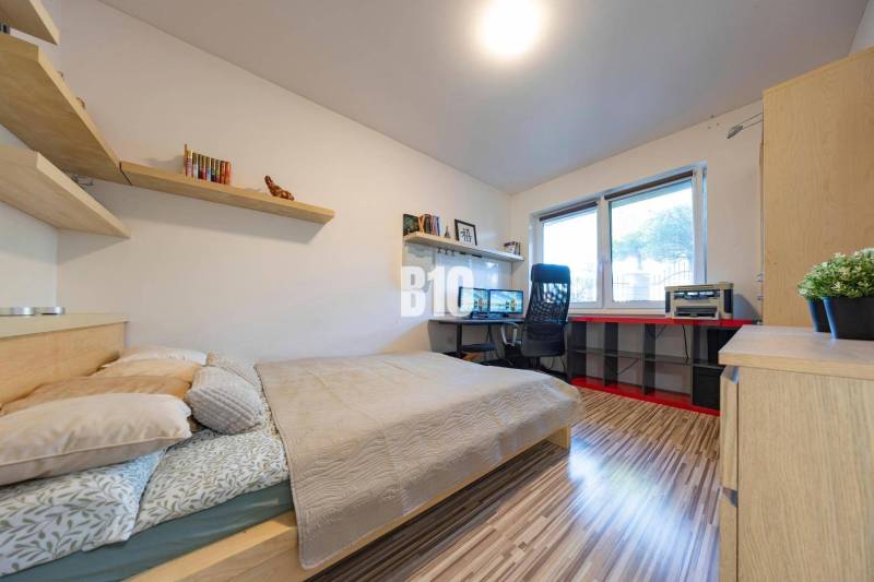 Tri Vody - 4-izbový rodinný dom s bazénom | Most pri Bratislave – Baza - Spálňa v rodinnom dome s pracovným stolom, policami a podlahou s dreveným dekorom.