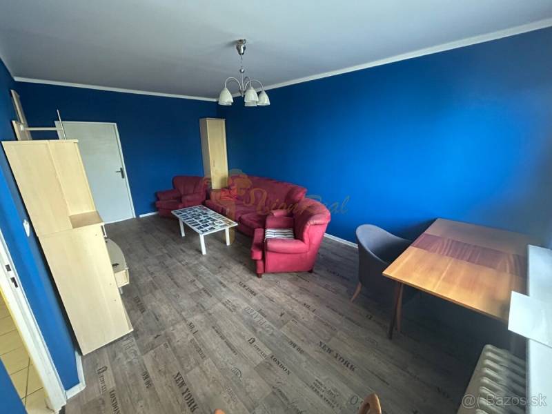Veľký 2-izb. byt na ul. Vranovská, Petržalka, lodžia, 4.p./7 - Modrá garsónka s červenou pohovkou, stolíkom a podlahou s dreveným dekorom.