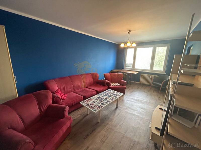 Veľký 2-izb. byt na ul. Vranovská, Petržalka, lodžia, 4.p./7 - Garsónka so sedačkou, modrou stenou a podlahou s dreveným dekorom.