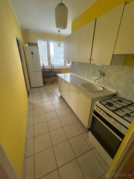 Veľký 2-izb. byt na ul. Vranovská, Petržalka, lodžia, 4.p./7 - Kuchyňa v garsónke so žltými stenami, bielymi skrinkami a sporákom.