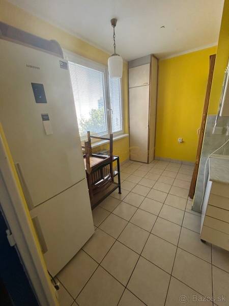 Veľký 2-izb. byt na ul. Vranovská, Petržalka, lodžia, 4.p./7 - Kuchyňa garsónky so žltými stenami, chladničkou a dlažbou na podlahe.