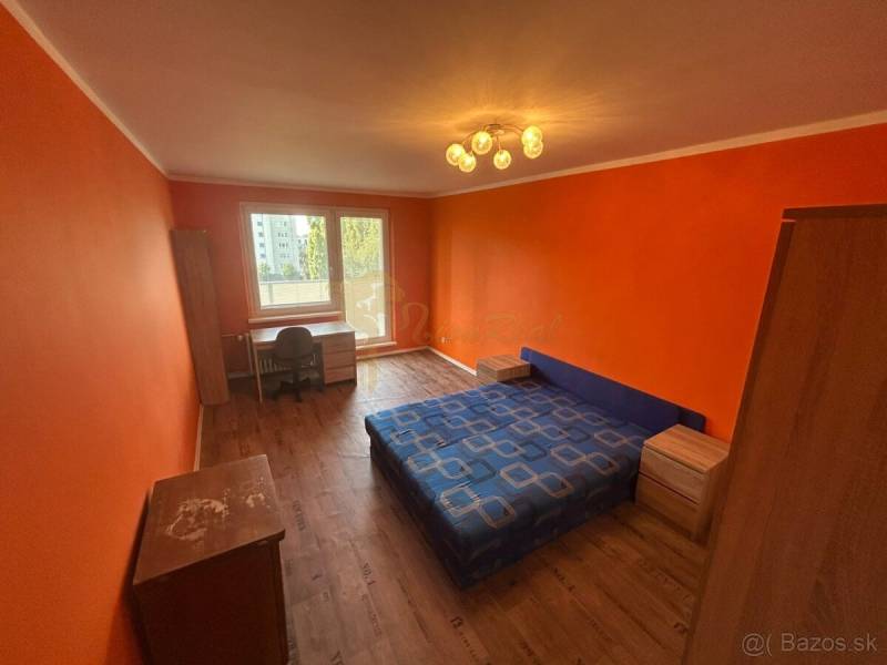 Veľký 2-izb. byt na ul. Vranovská, Petržalka, lodžia, 4.p./7 - Oranžové steny, lôžko, podlaha s dreveným dekorom a stôl v garsónke.