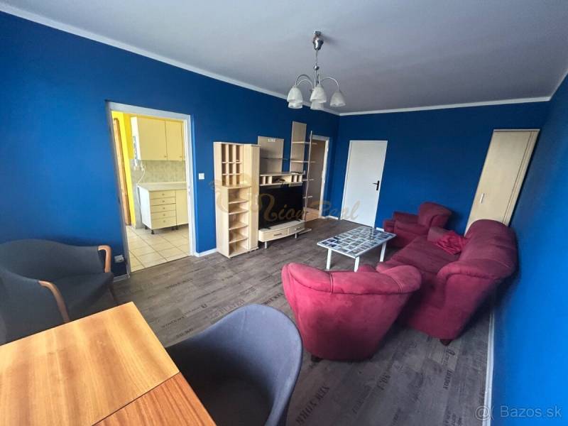 Veľký 2-izb. byt na ul. Vranovská, Petržalka, lodžia, 4.p./7 - Izba s modrými stenami, červeným nábytkom a podlahou s dreveným dekorom.