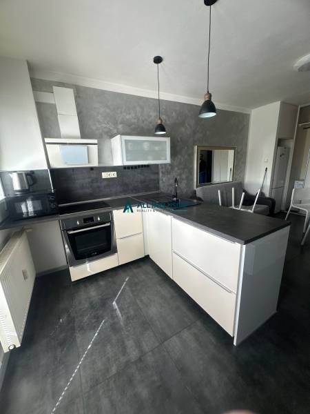 Stavbárska ulica,2-garsónka na prenájom - Kuchyňa v dvojgarsónke s tmavou pracovnou doskou, sivou stenou a závesným osvetlením.