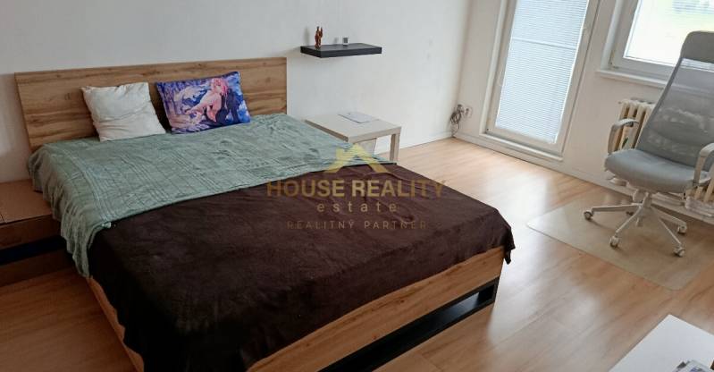 Pekný 1 izbový byt, Tilgnerova ulica, Bratislava IV. Karlova Ves - Spálňa v 1-izbovom byte s posteľou, kreslom a podlahou s dreveným dekorom.