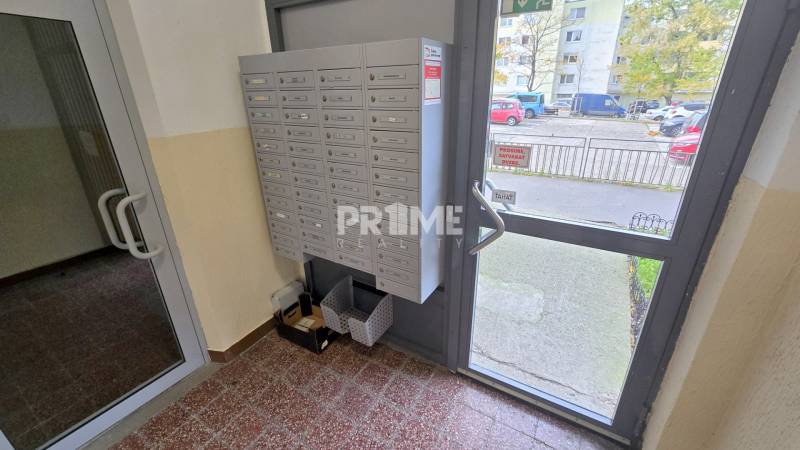 Príjemný 1i byt, zariadený, pivnica, Drobného ul., Dúbravka - Vstup do bytového domu s poštovými schránkami, sklenenými dverami a výhľadom na parkovisko.