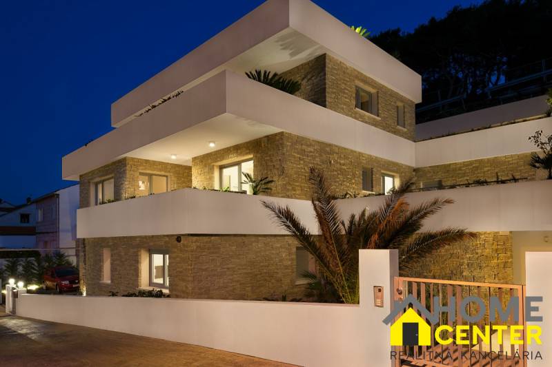 KRÁSNA MODERNÁ VILA  /400 m²/ s výhľadom na more, ostrov BRAČ - Exteriér Vily v meste Bol so svetlými terasami a kamennými stenami za súmraku.