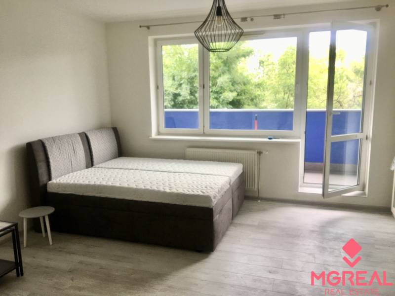 PRENÁJOM 1i byt s Loggiou, Tomášikova ul., Ružinov - Svetlá izba s posteľou, otvoreným balkónom a podlahou s dreveným dekorom.