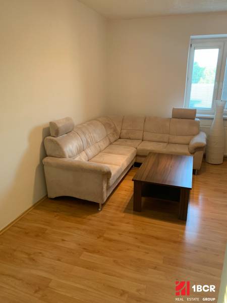 PRIESTRANNÝ 2-IZB BYT V UZAVRETOM AREÁLI, MIEROVÁ KOLÓNIA, NOVÉ MESTO - Obývacia izba v 2-izbovom byte s rohovou sedačkou a podlahou s dreveným dekorom.