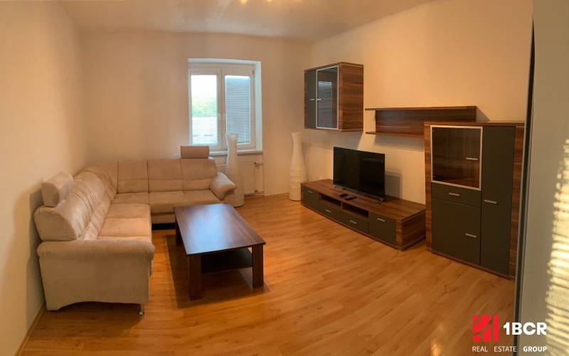 PRIESTRANNÝ 2-IZB BYT V UZAVRETOM AREÁLI, MIEROVÁ KOLÓNIA, NOVÉ MESTO - Obývacia izba s béžovou sedačkou, TV a dreveným dekorom v 2-izbovom byte.