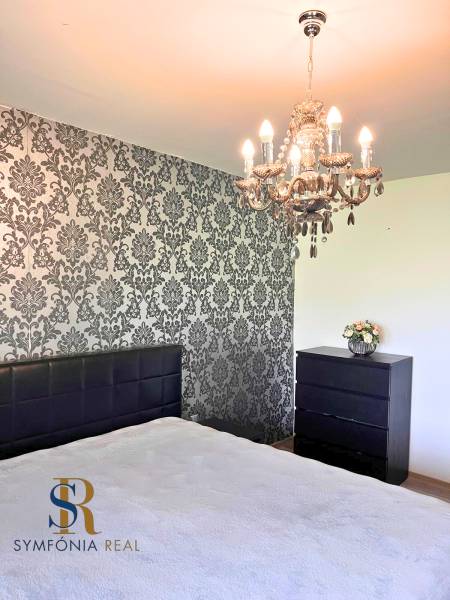 Rodinný dom v obci Dubová s 920m2 rozsiahlym pozemkom  - Spálňa s lustrom a tapetovou stenou v rodinnom dome. Podlaha s dreveným dekorom.