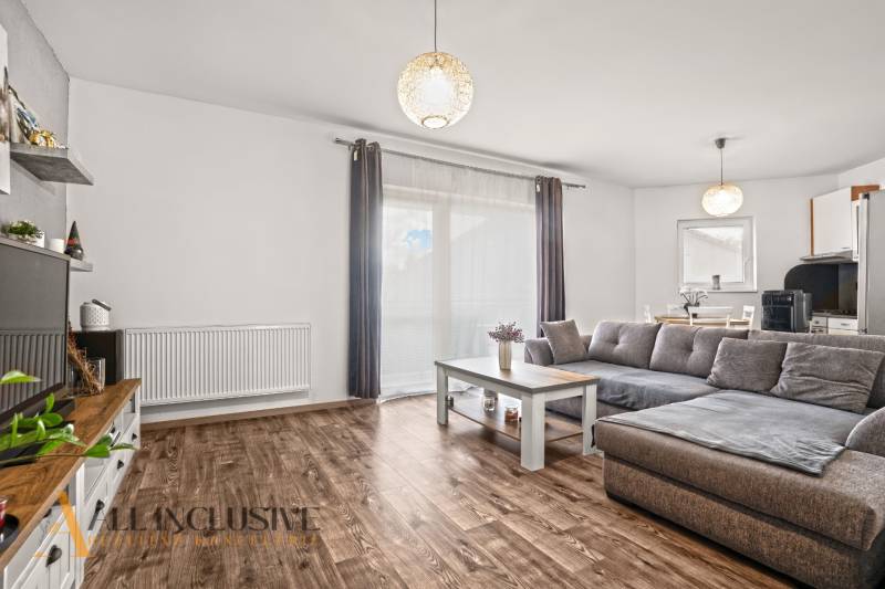 NA PREDAJ 2-IZBOVÝ BYT S 2 BALKÓNMI, DUNAJSKÁ STREDA - Obývacia izba v 2-izbovom byte s podlahou s dreveným dekorom a sivou sedačkou.