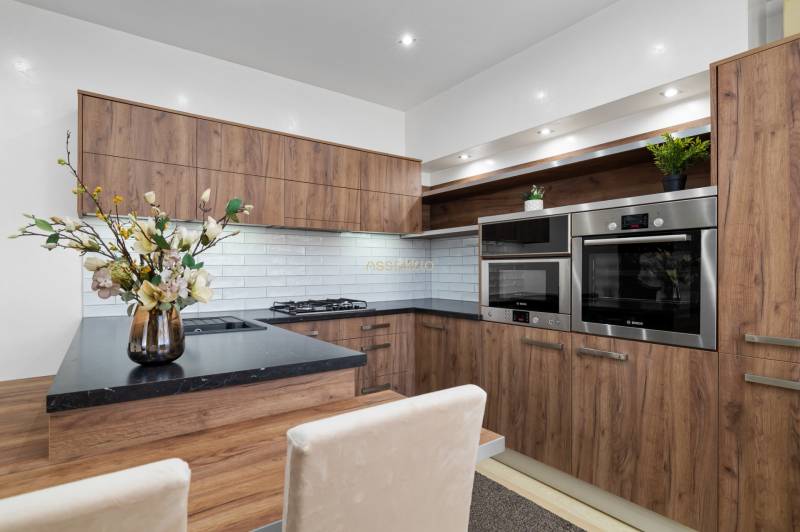 PREDAJ-2 IZBOVÝ BYT-KOMPLETNÁ REKONŠTRUKCIA - RUŽINOV - Kuchyňa v 2-izbovom byte, drevený dekor, biele obklady, vstavané spotrebiče.