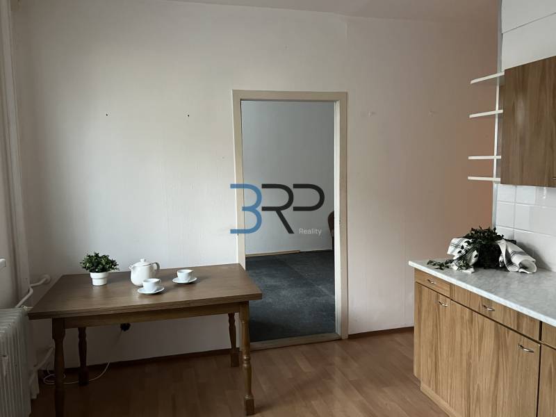 REZERVOVANÝ! Na predaj 2izbový byt v meste Senica - Kuchyňa v 2-izbovom byte s podlahou v drevenom dekore, stolom a riadom.