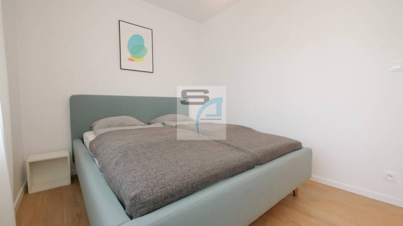 2-izbový byt s terasou 15 m² a parkovaním v tichej časti Bratislavy - Spálňa s posteľou a minimalistickou dekoráciou v 2-izbovom byte, podlaha s dreveným dekorom.