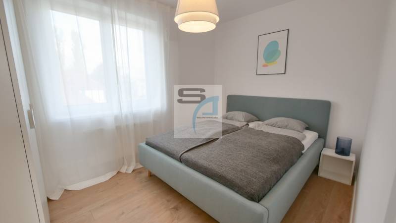 2-izbový byt s terasou 15 m² a parkovaním v tichej časti Bratislavy - Spálňa s veľkou posteľou, záclonami a podlahou s dreveným dekorom v 2-izbovom byte.