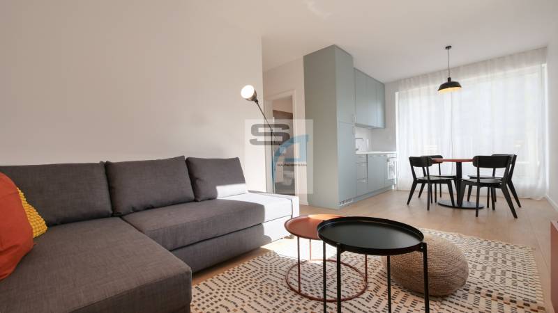 2-izbový byt s terasou 15 m² a parkovaním v tichej časti Bratislavy - Obývacia izba v 2-izbovom byte s pohovkou, jedálenským stolom a podlahou s dreveným dekorom.