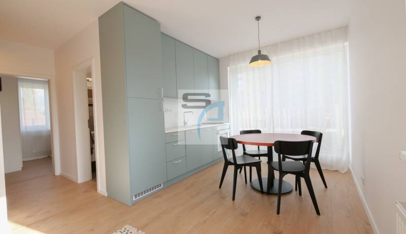 2-izbový byt s terasou 15 m² a parkovaním v tichej časti Bratislavy - Jedálenský kút so stolom a stoličkami, zabudovanými skrinkami a podlahou s dreveným dekorom.