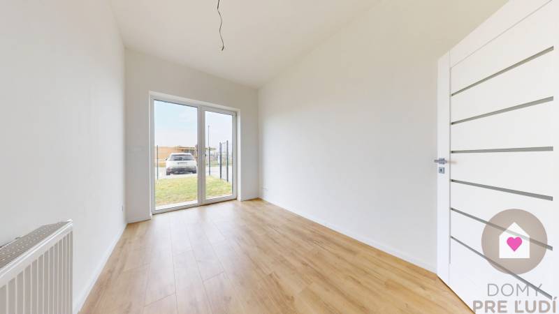 3i. BYT SO ZÁHRADOU +TEP. ČERPADLO, KLIMATIZÁCIA A ŽALÚZIE V CENE - Priestranná miestnosť s bielymi stenami a drevenou podlahou v 3-izbovom byte.