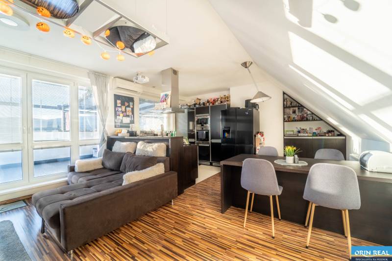 Rezervovaný!!! 2izb + terasa byt Vajanského Modra 93,8m2 - Obývačka s kuchyňou v 2-izbovom byte s podlahou s dreveným dekorom a pohodlnou sedačkou.