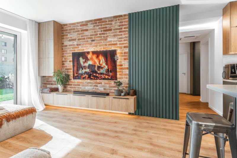 PRENÁJOM 3 izbový byt s predzáhradkou, BORY PROMENÁDA - Obývačka v 3-izbovom byte s tehlovou stenou, krbom a podlahou s dreveným dekorom.