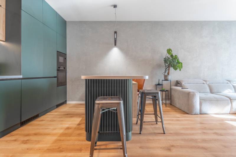 PRENÁJOM 3 izbový byt s predzáhradkou, BORY PROMENÁDA - Kuchyňa v 3-izbovom byte s ostrovčekom, kovovými stoličkami a podlahou s dreveným dekorom.