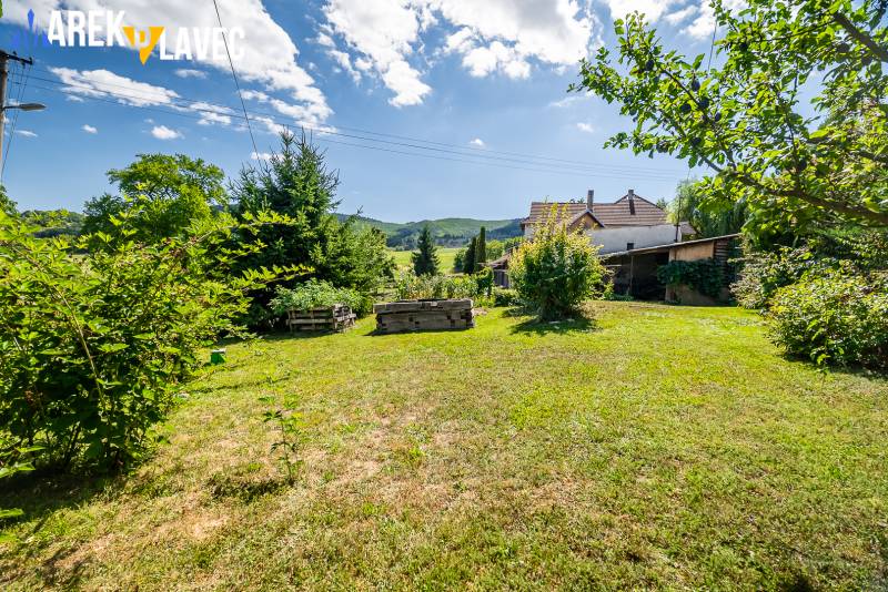 Na predaj: Rodinný dom Slatinské Lazy s očarujúcou atmosférou - Záhrada rodinného domu v Slatinských Lazoch s trávnikom a výsadbou, obklopená stromami.