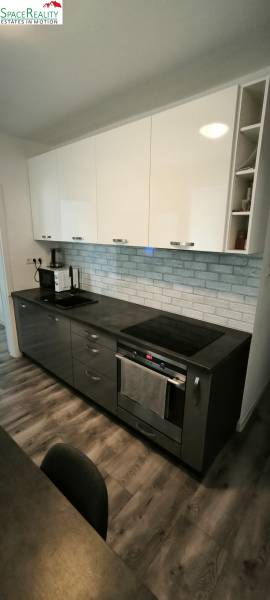 Prenajmeme 3 izb  byt na Korytnickej ulici - Kuchyňa v 3-izbovom byte s tmavými skrinkami a podlahou s dreveným dekorom.