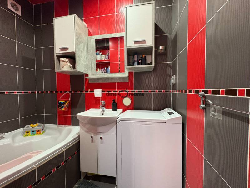 Na predaj: Investičný 3 izb.byt + murovaná PIVNICA - Kúpeľňa v 3-izbovom byte so sprchovacím kútom a práčkou, červené a sivé obklady.