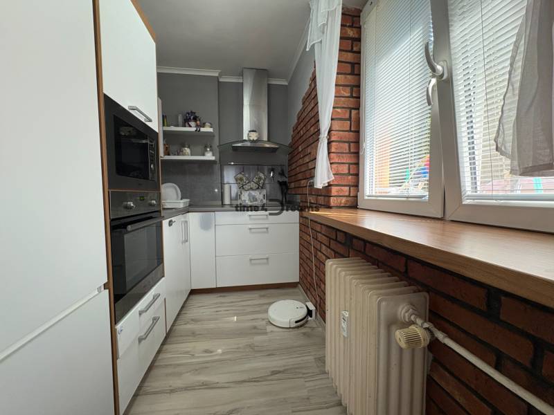 Na predaj: Investičný 3 izb.byt + murovaná PIVNICA - Kuchyňa v 3-izbovom byte s bielymi skrinkami, tehlovým obkladom a veľkým oknom.