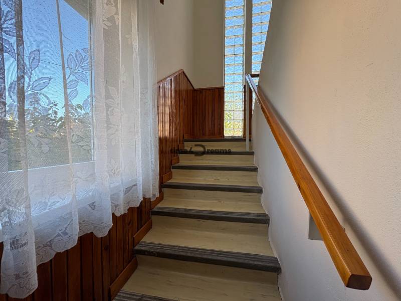 Na predaj: Rodinný dom v meste Levice - Schodisko s dreveným obkladom a zábradlím, veľké okno s kvetinovým závesom.