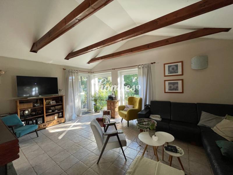 PREDAJ krásny 6 izb. rod. dom prepojený s prírodou - Obývacia izba s trámovým stropom, dlažbou, čiernou sedačkou a výhľadom do záhrady v rodinnom dome.