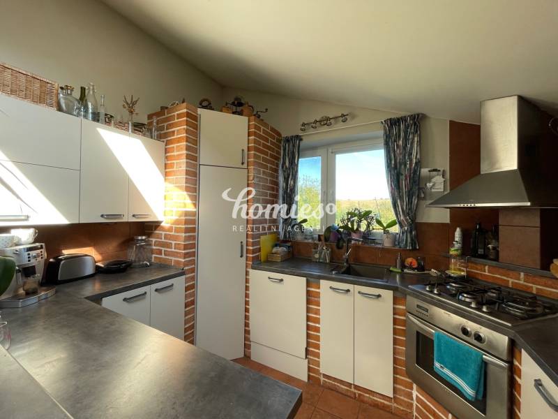 PREDAJ krásny 6 izb. rod. dom prepojený s prírodou - Kuchyňa v rodinnom dome má tehlový obklad, biele skrinky a plynový sporák.