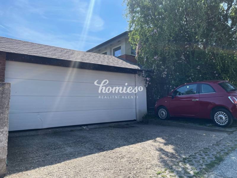 PREDAJ krásny 6 izb. rod. dom prepojený s prírodou - Brána do garáže pri rodinnom dome v Lehote, vedľa je zaparkované červené auto.