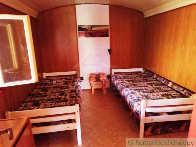Chata nad kúpeľmi Dudince s vlastným pozemkom - Drevený interiér chaty s dvoma lôžkami a podlahou s dreveným dekorom.