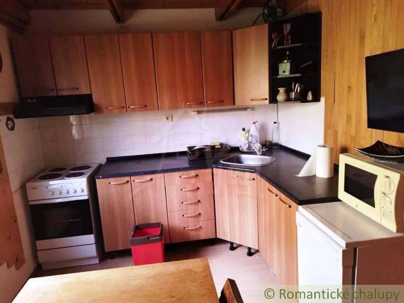 Chata nad kúpeľmi Dudince s vlastným pozemkom - Kuchyňa v chate s podlahou s dreveným dekorom, varnou doskou a mikrovlnkou.