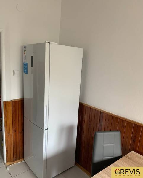 Priestranný 2-izbový byt (62 m²) s Lodžiou, Nobelova – Nové Mesto - Kuchyňa v 2-izbovom byte s bielou chladničkou a drevenými obkladmi na stenách.