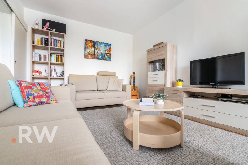 REWIN I Priestranný 3 izbový byt v tichej lokalite Senca - Obývačka s béžovým nábytkom v 3-izbovom byte, poličky, gauč a televízor.