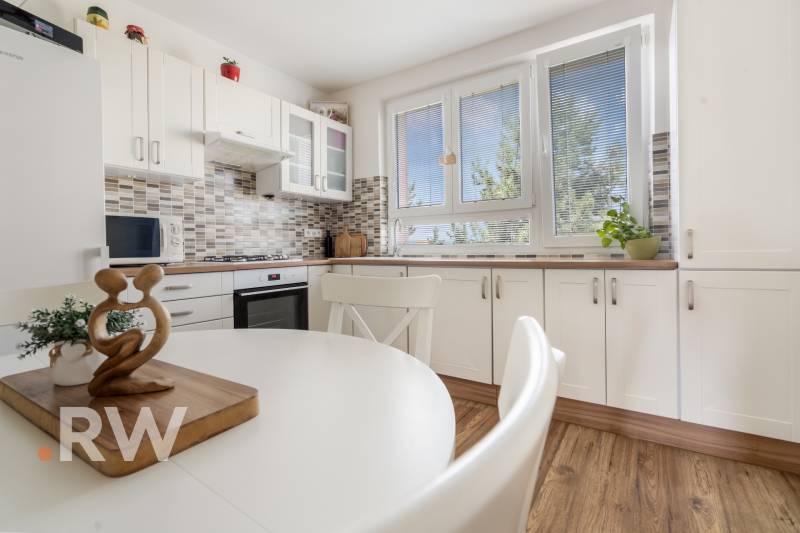 REWIN I Priestranný 3 izbový byt v tichej lokalite Senca - Kuchyňa v 3-izbovom byte s bielym nábytkom, jedálenský stôl a veľké okná.