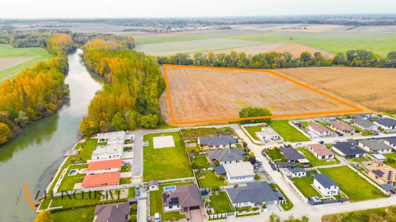 NA PREDAJ INVESTIČNÝ STAVEBNÝ POZEMOK, JAHODNÁ - Krajina v Jahodnej s developerskými pozemkami pri rieke a blízkymi domami.