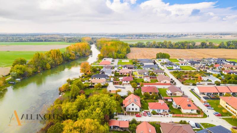 NA PREDAJ INVESTIČNÝ STAVEBNÝ POZEMOK, JAHODNÁ - Pohľad na Developerské pozemky v Jahodnej pri rieke, obklopené zeleňou a domami.