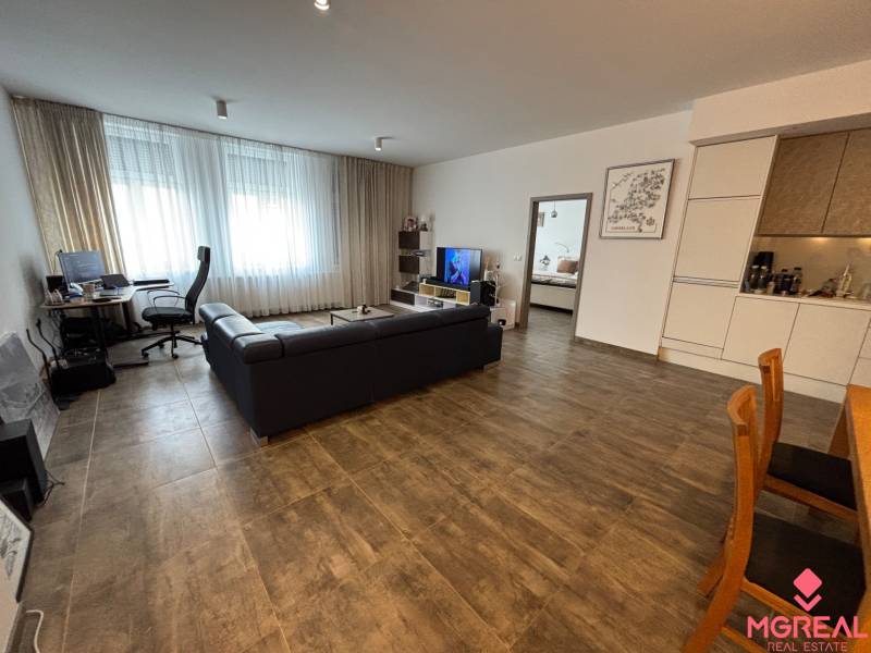 Veľký 96 m2  2 izbový byt s garážovým státím Topoľčany Centrum  - Obývacia miestnosť 2-izbového bytu s tmavým gaučom a pracovným kútom.