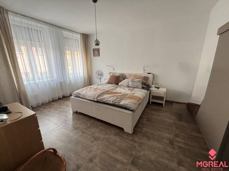 Veľký 96 m2  2 izbový byt s garážovým státím Topoľčany Centrum  - Spálňa v 2-izbovom byte s veľkými oknami, posteľou a podlahou s dreveným dekorom.