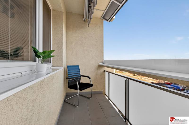 REZERVOVANÉ Predaj moderný 1-izbový byt, 45,24m2, Bratislava IV - Balkón na Milana Marečka v Bratislave - Devínskej Novej Vsi s kreslom a rastlinou.