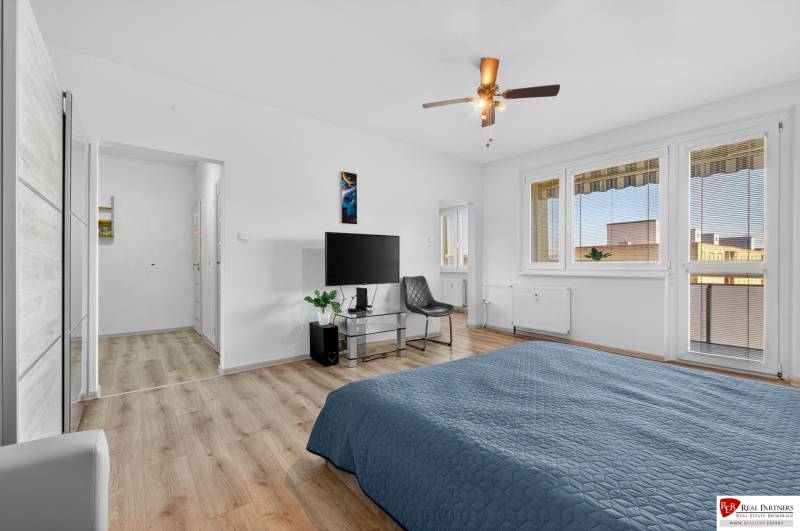 REZERVOVANÉ Predaj moderný 1-izbový byt, 45,24m2, Bratislava IV - Spálňa v 1-izbovom byte s televízorom, kreslom a podlahou s dreveným dekorom.
