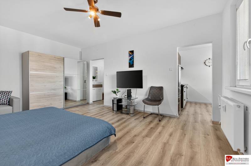 REZERVOVANÉ Predaj moderný 1-izbový byt, 45,24m2, Bratislava IV - Jednoizbový byt s podlahou s dreveným dekorom, posteľou a televízorom na stene.