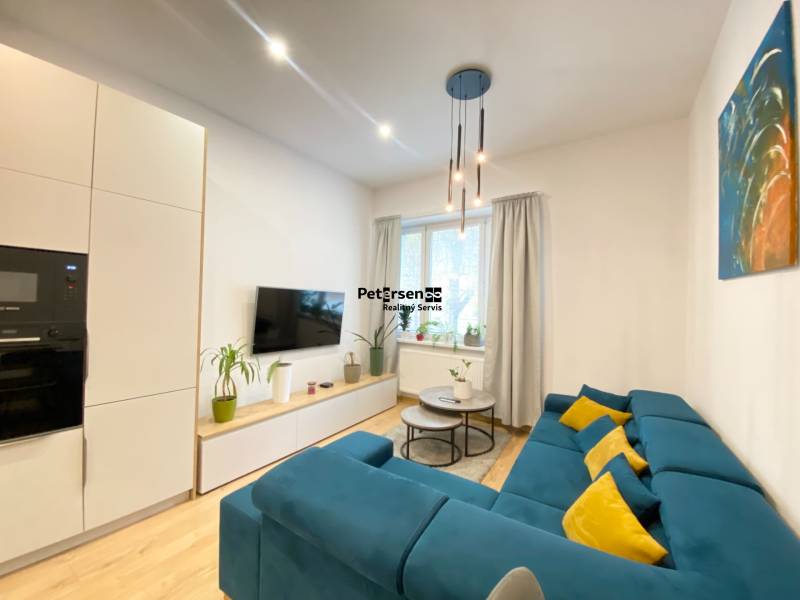 NA PRENÁJOM ŠTÝLOVÝ 2-IZBOVÝ BYT V CENTRE KOŠÍC, DREVNÝ TRH - Obývačka v 2-izbovom byte s modrou sedačkou a podlahou s dreveným dekorom.