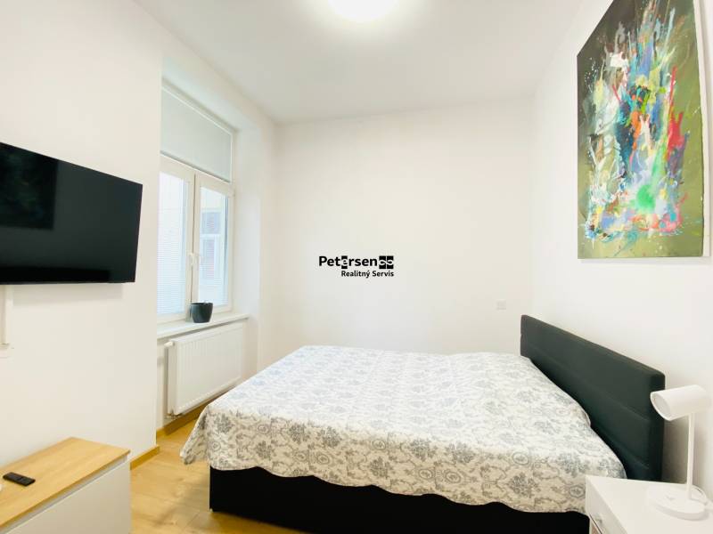 NA PRENÁJOM ŠTÝLOVÝ 2-IZBOVÝ BYT V CENTRE KOŠÍC, DREVNÝ TRH - Spálňa s televízorom, posteľou a abstraktným obrazom v 2-izbovom byte.