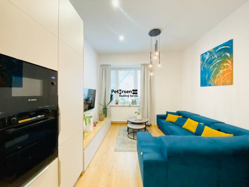 NA PRENÁJOM ŠTÝLOVÝ 2-IZBOVÝ BYT V CENTRE KOŠÍC, DREVNÝ TRH - Obývacia izba s modrým gaučom, farebným obrazom a podlahou s dreveným dekorom v 2-izbovom byte.