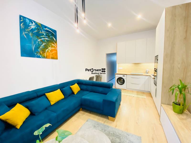 NA PRENÁJOM ŠTÝLOVÝ 2-IZBOVÝ BYT V CENTRE KOŠÍC, DREVNÝ TRH - Obývacia izba 2-izbového bytu s modrou sedačkou a podlahou s dreveným dekorom.